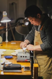 Asian Master luthier lute maker artisan both hands performing bend controller purfling strips process in iron tool for a new raw back and front plates of classic handmade violin in his workshop in Cre...