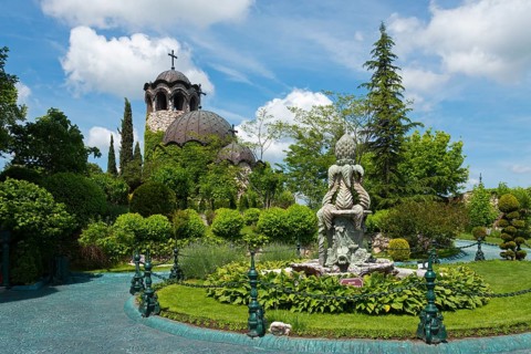 Church with dome next to a well-tended garden with sculpture and blue waterway