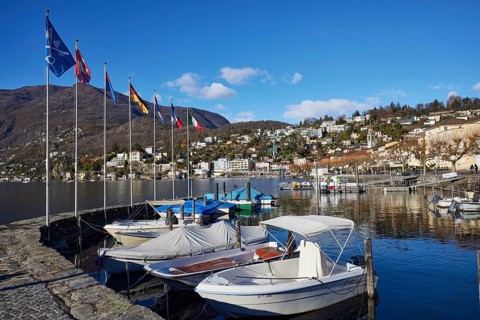 Motorboats and stone wall with flags in the harbour of Ascona