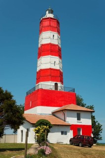A red and white striped lighthouse next to a house with a vehicle in front of it under a clear sky