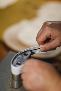 Unrecognizable luthier lute maker artisan both hands performing bend controller purfling strips process in iron tool for a new raw back and front plates of classic handmade violin in his workshop in C...