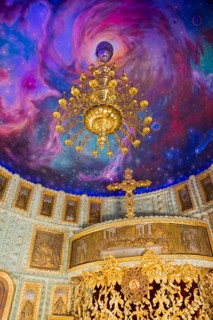 An opulent chandelier in a church with an illusionistic galaxy painted on the ceiling