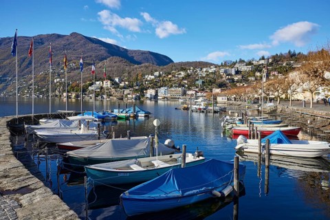 Motorboats and stone wall with flags in the harbour of Lake Maggiore in the bay of Ascona
