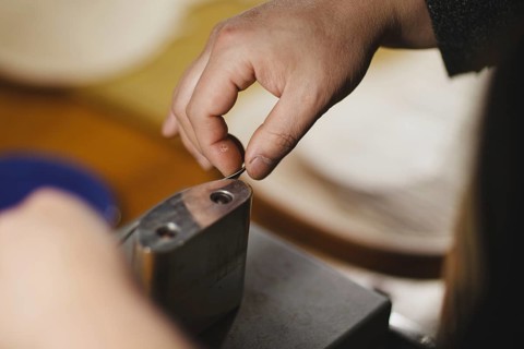 Unrecognizable luthier lute maker artisan hands in his workshop performing bend controller purfling strips process in iron tool for a new raw back and front plates of classic handmade violin in Cremon...