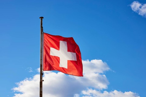 Swiss flag on a flagpole in front of a blue sky with white clouds in Ascona