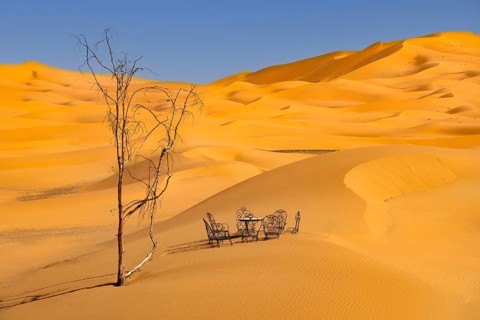 Dead tree and cast iron garden table and lawn chairs in sand dunes of Erg Chebbi