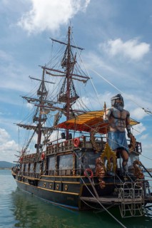 A large sailing ship with many masts and a pirate statue on board is anchored in the sea