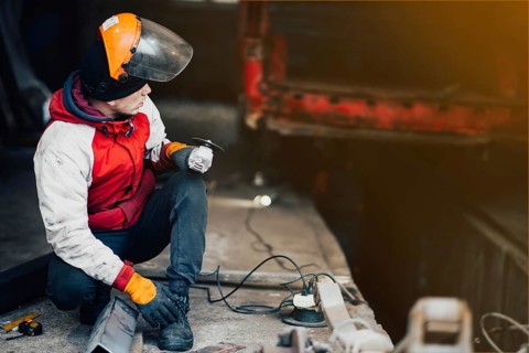 Man worker in a uniform and a mask works with a grinder