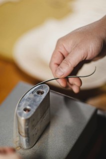 Unrecognizable luthier lute maker artisan both hands performing bend controller purfling strips process in iron tool for a new raw back and front plates of classic handmade violin in his workshop in C...