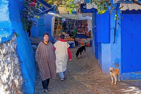 Muslim man wearing traditional djellaba and grocery shop in alleyway in blue medina
