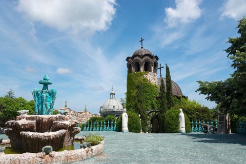 A chapel with religious statues and water basins surrounded by inviting greenery