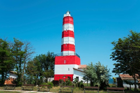 Red and white striped lighthouse surrounded by trees and a meadow under a blue sky