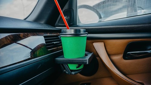 Cardboard cup of coffee inside a car in a passenger's hand