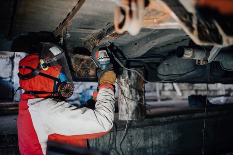 Male car service worker cleans the bottom of the car body with a grinder. Waterproofing metal of a car body