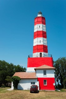 Red and white lighthouse against a clear blue sky with a red car in front of it