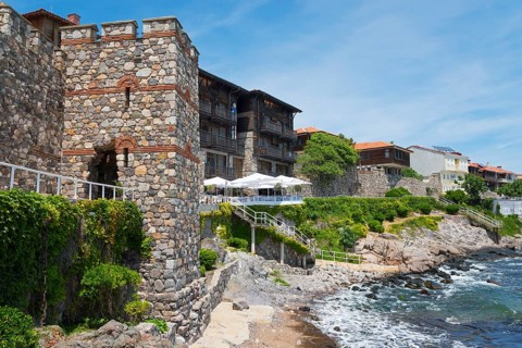 Traditional stone house on a rocky coastline with blue sky and sea in the background