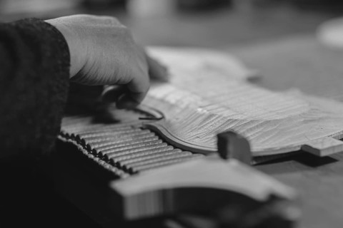 Violinmaker artisan hand in his workshop hold purfling fillet made of evony and ivory or pear wood ready to be inserted in the carved all around the shape for aesthetic touch and prevent cracking
