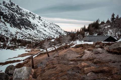 A serene winter landscape with a cabin, snow-covered mountain, and wooden fence at dusk. Poland,
