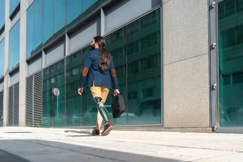 Rear view of a young businessman with amputee leg walking along a street