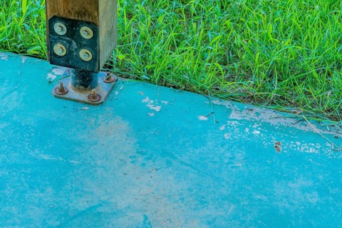 Square wooden support column attached to concrete base using metal anchor plate