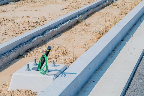 Electrical wiring protruding from newly installed lamppost base next to curb at construction site