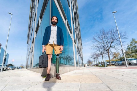 Businessman with prosthetic leg holding a laptop bag outside a financial building in the city