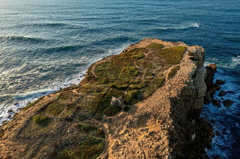 Drone view of rocky headland and blue sea waves at sunset. Ocean tide beat and splash in summer