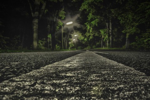 An empty street at night, focussed on the central reservation and surrounded by dark trees, Haan,