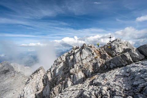 Mountaineer on the rocky summit of the Watzmann Mittelspitze with summit cross, Watzmann crossing,