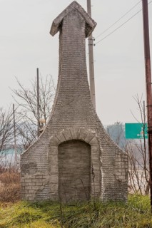 Small wire-frame and stucco building resembling a church in grassy area next to highway