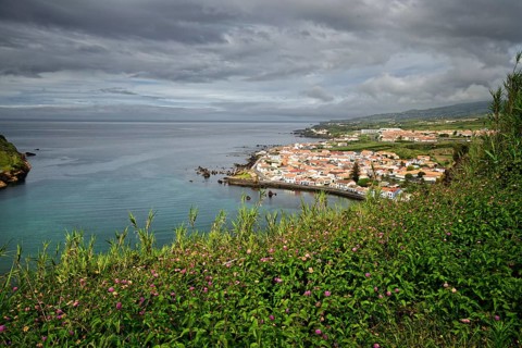 View of the town of Horta surrounded by green hills and cliffs under a cloudy sky, Monte da Guia,