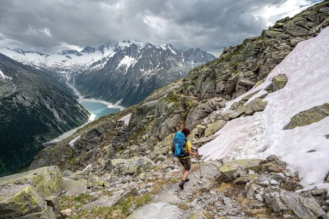 Mountaineer on hiking trail with snow, view of Schlegeisspeicher, glaciated rocky mountain peaks