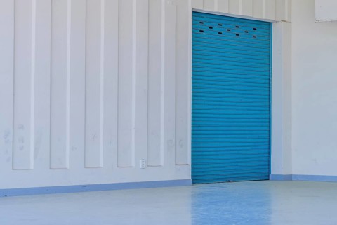 Large blue metal door in white wall reflecting onto concrete floor of amphitheater in urban public