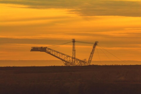 Silhouette of a large conveyor bridge against the orange-coloured evening sky, open-cast lignite