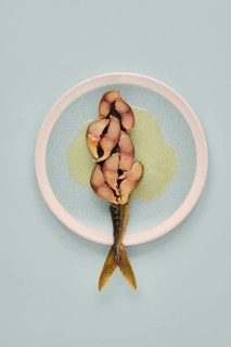 Sliced mackerel on a plate revealing its pinkish inner flesh against the darker outer skin. The