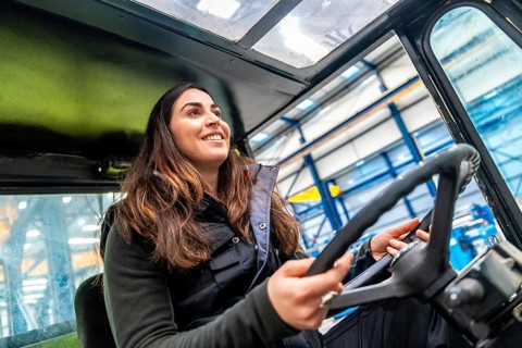 Low angle view close-up of a happy woman driving a forklift in a factory