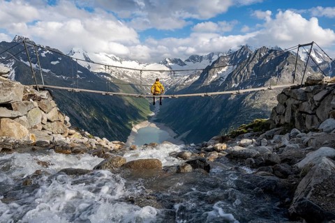 Mountaineer sitting on a suspension bridge over a mountain stream Alelebach, picturesque mountain