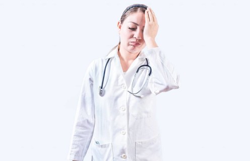 Exhausted female doctor with hand on forehead. Tired young female doctor with hand on forehead