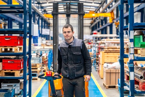 Frontal view of a male worker walking among shelves with handcart in a warehouse