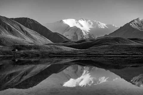 White glaciated and snowy mountain peak Lenin Peak at sunset, mountains reflected in a lake between