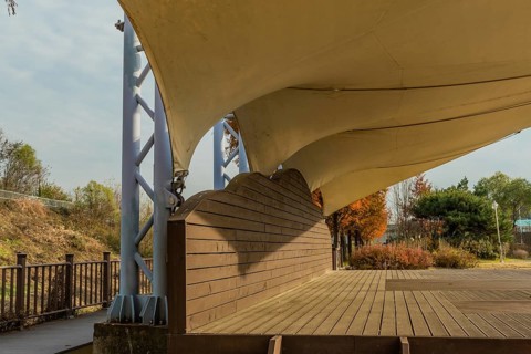Closeup side view of wooden outdoor stage with white canvas awning in public park