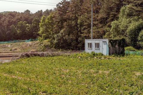 Small metal storage building in field in front of treeline