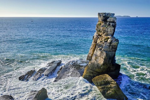 Blue sea waves beat against Nau dos Corvos or Crows nest rock near Peniche peninsula, Portugal at