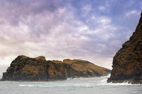 Rocky island 'Iieu Deitado' under a dramatic cloudy sky with gentle waves at the base, Iieu
