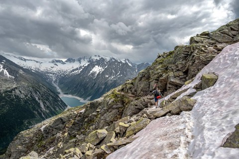 Mountaineer on hiking trail with snow, view of Schlegeisspeicher, glaciated rocky mountain peaks