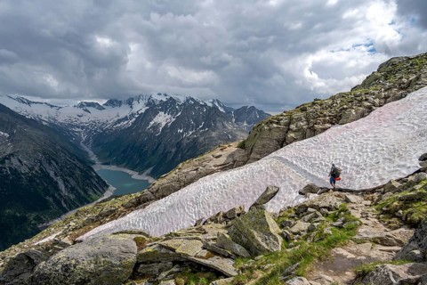 Mountaineer on hiking trail with snow, view of Schlegeisspeicher, glaciated rocky mountain peaks