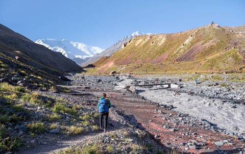 Hiker iTal with river Achik Tash between high mountains, mountain landscape with peak Pik Lenin,