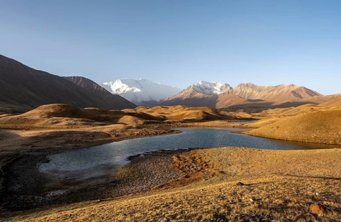 White glaciated and snowy mountain peak Pik Lenin at sunrise, mountains reflected in a lake between