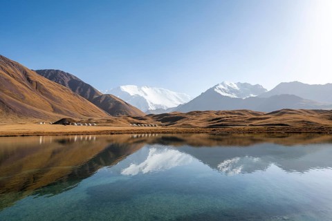 White glaciated and snow-covered mountain peak Pik Lenin at sunset, mountains reflected in Lake