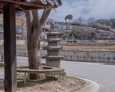 Five story concrete pagoda next to tree in public park on corner of rural street